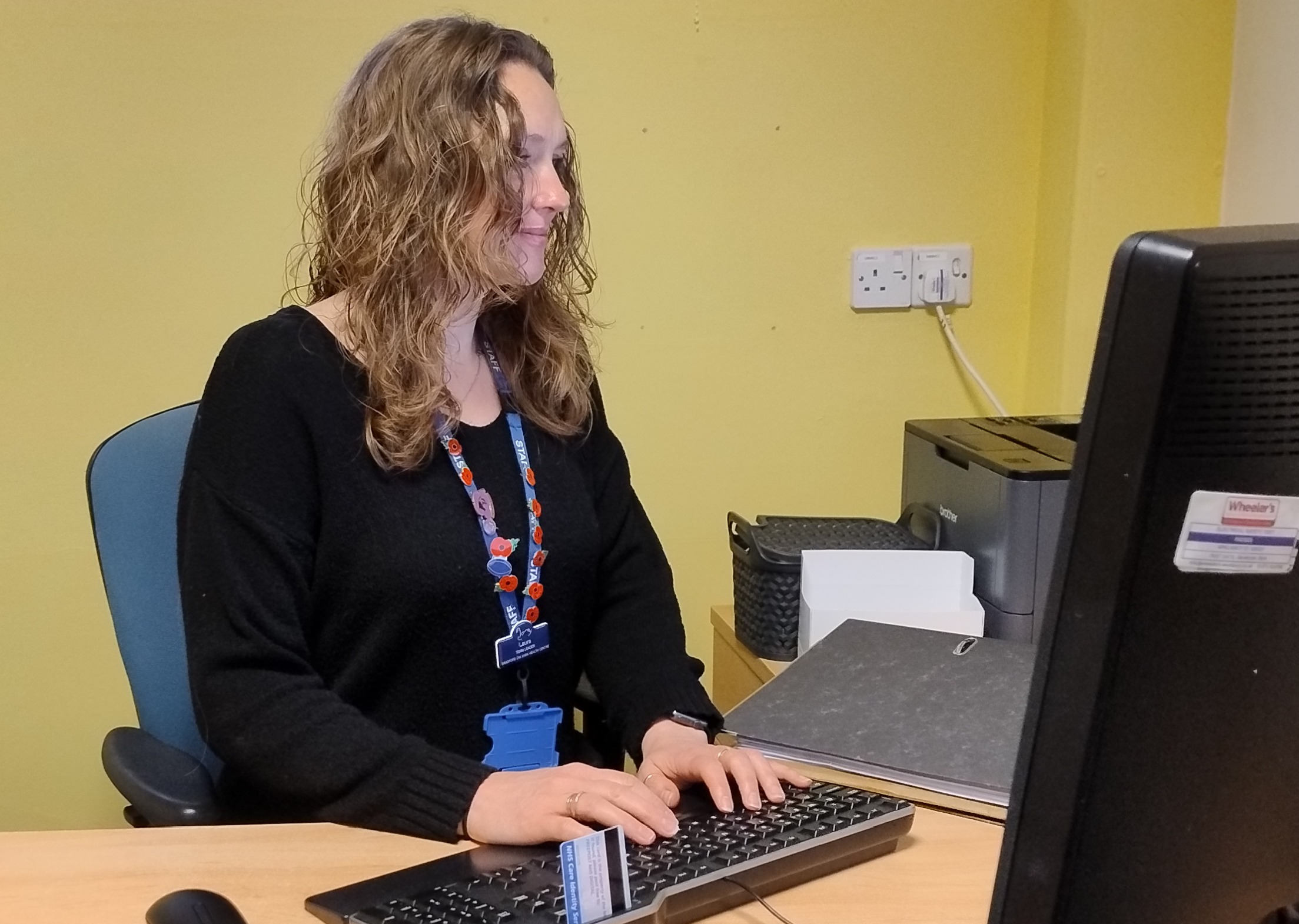 Laura sits at a desk with a keyboard and a computer.