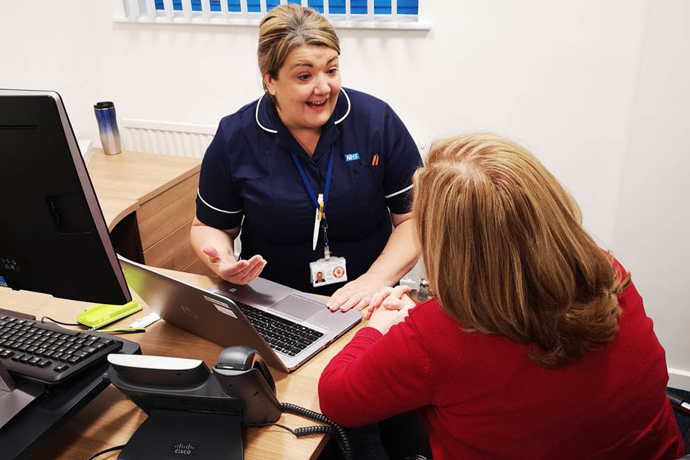 Community midwife Juie Haigh speaks to a patient while working at a computer