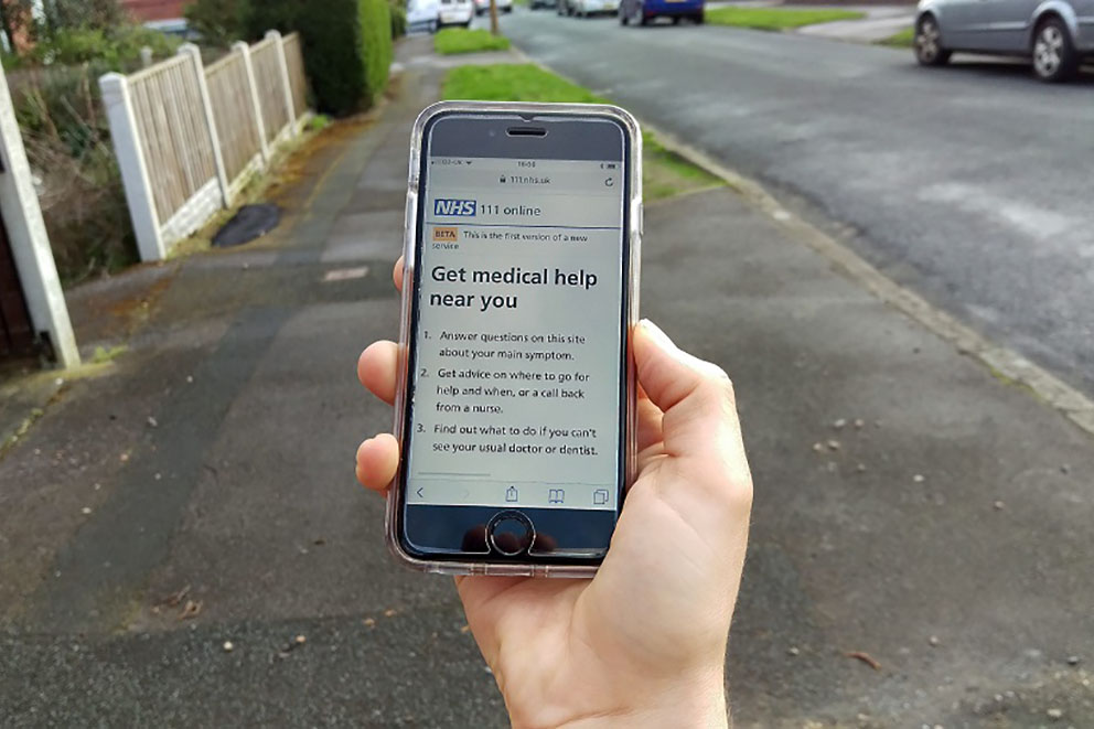 Hand of someone walking down road holding phone with 111 Online up on the screen