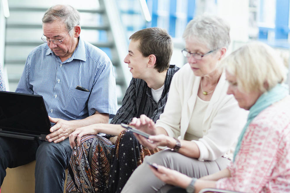 A group of male and female patients look at laptops and mobile devices