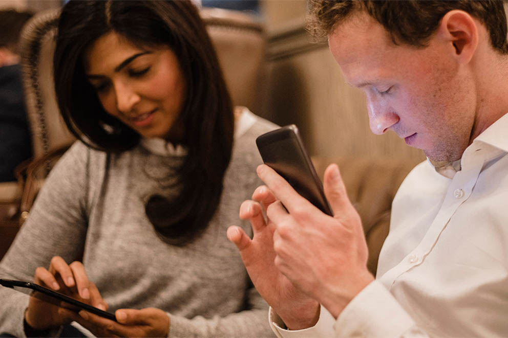 A male and female sit next to each other using their smartphones
