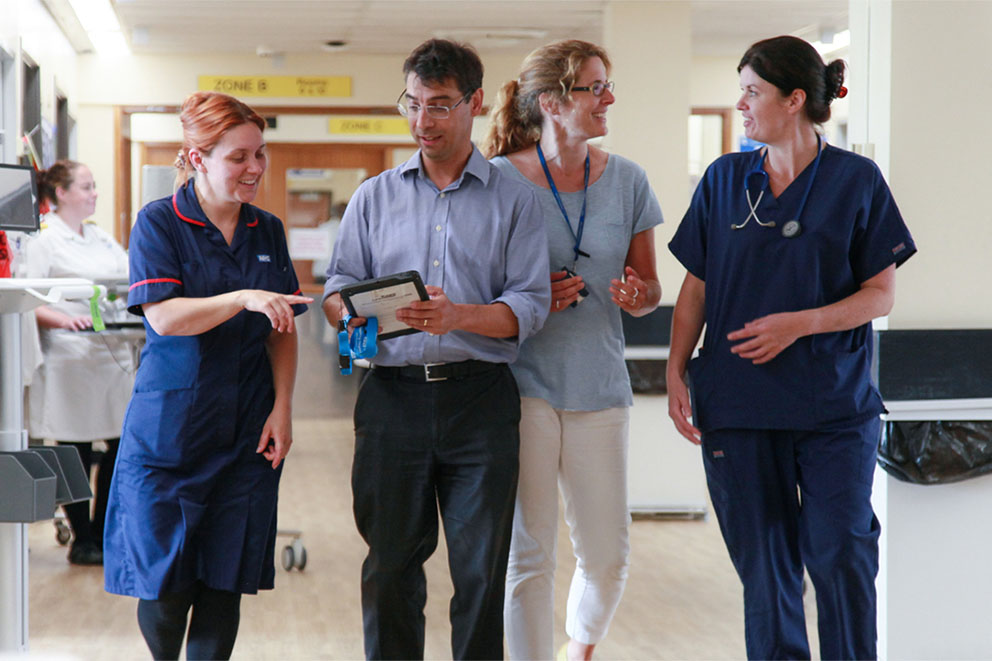 Picture with four clinical staff walking down the aisle of ward 30, using Wirral Millennium to discuss a patient treatment, Wirral University Teaching Hospital