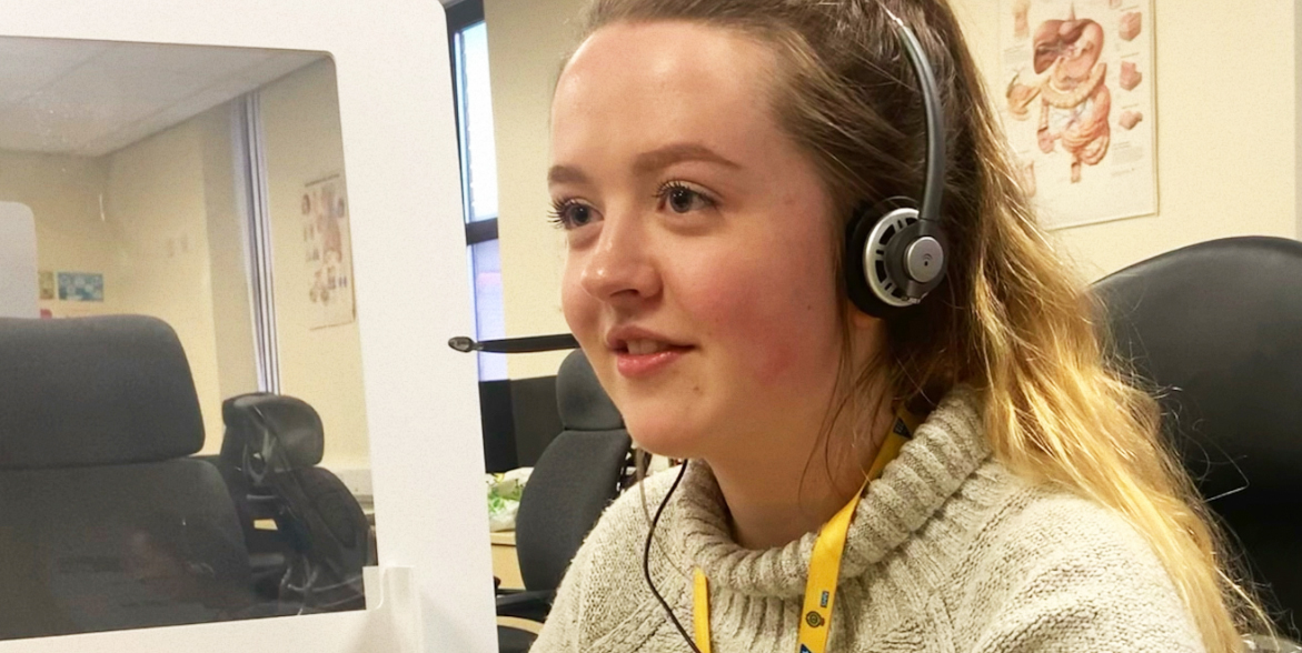 photograph of call handler Gina Gill at her desk wearing head set.