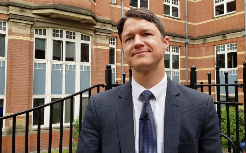 Daniel Ray wearing a suit standing in front of brickwork office building