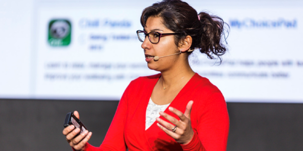 A side-on image of Dr Indra Joshi presenting in front of a large screen with a Powerpoint presentation