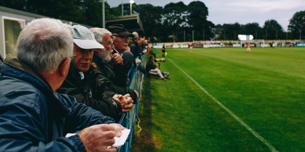 Some men in their 60s or 70s standing watching a non-league football match
