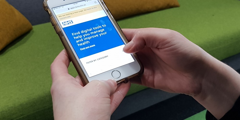 A person holding a smartphone accessing an NHS mental health app