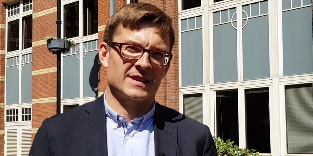 Head and shoulders photo of Nick Venters wearing glasses, suit and open neck shirt