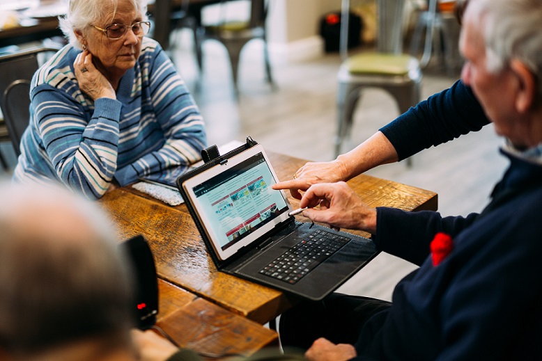 Elderly people being shown how to access healthcare info on a laptop